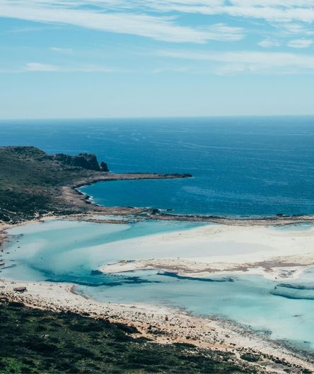 Blick von oben auf eine weitläufige, helle Sandlagune mit flachem, türkisblauem Wasser, die an ein tiefblaues Meer grenzt. Blick von oben auf eine weitläufige, helle Sandlagune mit flachem, türkisblauem Wasser, die an ein tiefblaues Meer grenzt.